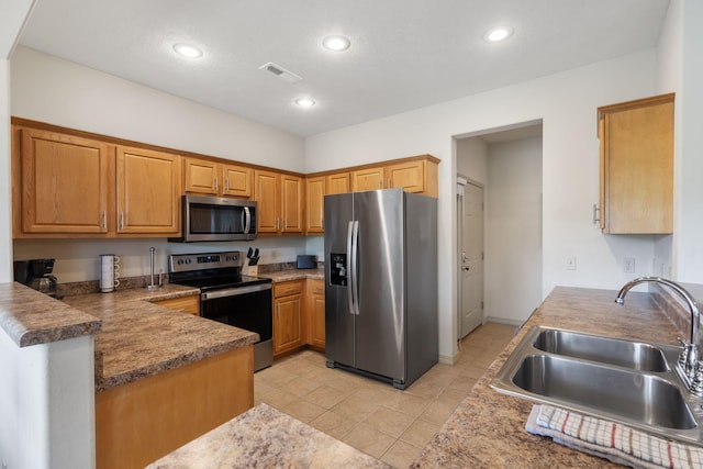 kitchen with appliances with stainless steel finishes, kitchen peninsula, sink, and light tile patterned floors