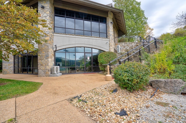 entrance to property with stone siding, ac unit, and a patio
