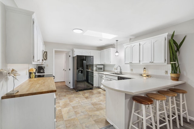 kitchen featuring black fridge, white cabinetry, hanging light fixtures, and a skylight