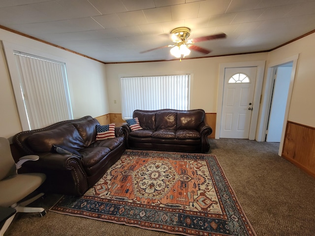 carpeted living room featuring wainscoting, a ceiling fan, ornamental molding, and wooden walls
