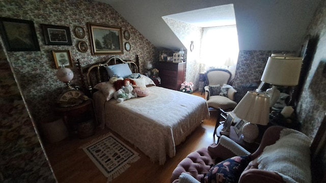 bedroom featuring vaulted ceiling, wood finished floors, and wallpapered walls