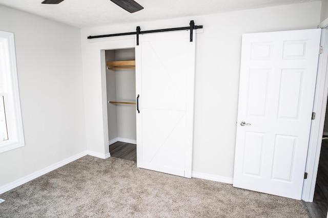 unfurnished bedroom featuring light carpet, ceiling fan, a barn door, and a closet