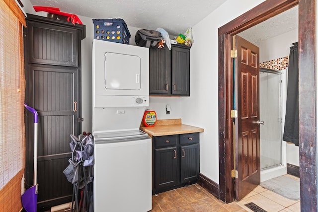 laundry area featuring stacked washer and clothes dryer, cabinets, light tile patterned floors, and a textured ceiling