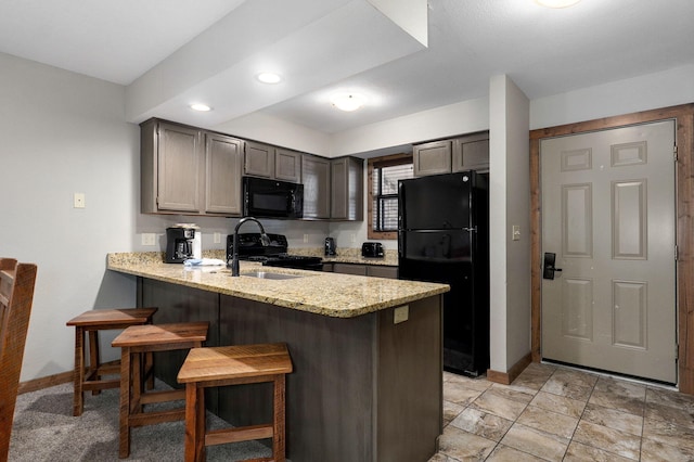 kitchen featuring a breakfast bar, light stone countertops, sink, kitchen peninsula, and black appliances