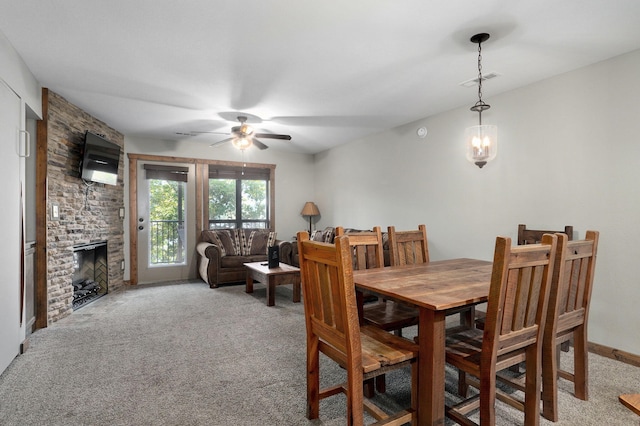 dining area with a stone fireplace, light colored carpet, and ceiling fan