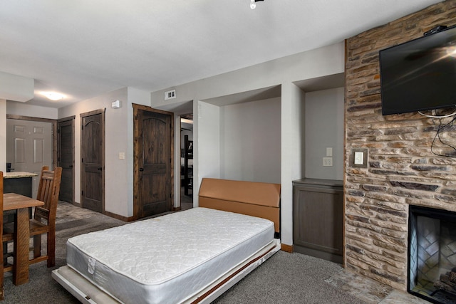 carpeted bedroom featuring two closets, a stone fireplace, and ensuite bath