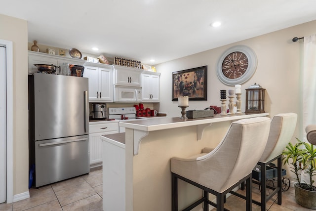 kitchen featuring a breakfast bar area, kitchen peninsula, white appliances, and white cabinetry