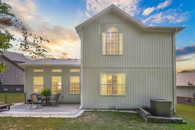 back house at dusk with a patio area, a yard, and central AC