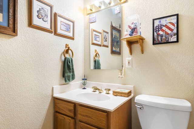 half bathroom with toilet, vanity, and a textured wall