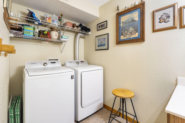 clothes washing area with light tile patterned flooring, separate washer and dryer, and a textured ceiling