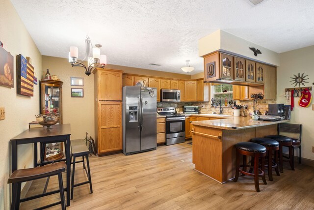 kitchen featuring stainless steel appliances, a peninsula, light wood-style floors, and a sink