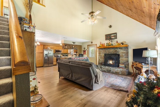 living room featuring ceiling fan, high vaulted ceiling, light hardwood / wood-style flooring, and a stone fireplace