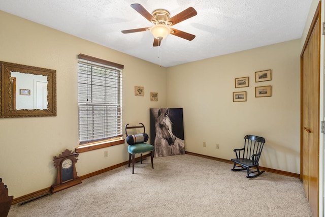 living area with a textured ceiling, ceiling fan, and light colored carpet