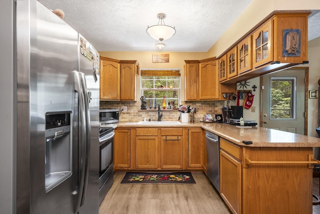 kitchen with sink, kitchen peninsula, backsplash, stainless steel appliances, and light hardwood / wood-style floors