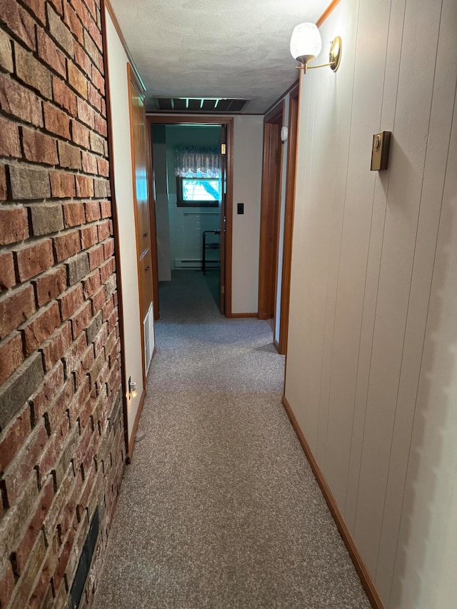 corridor featuring a textured ceiling, wooden walls, brick wall, and carpet flooring