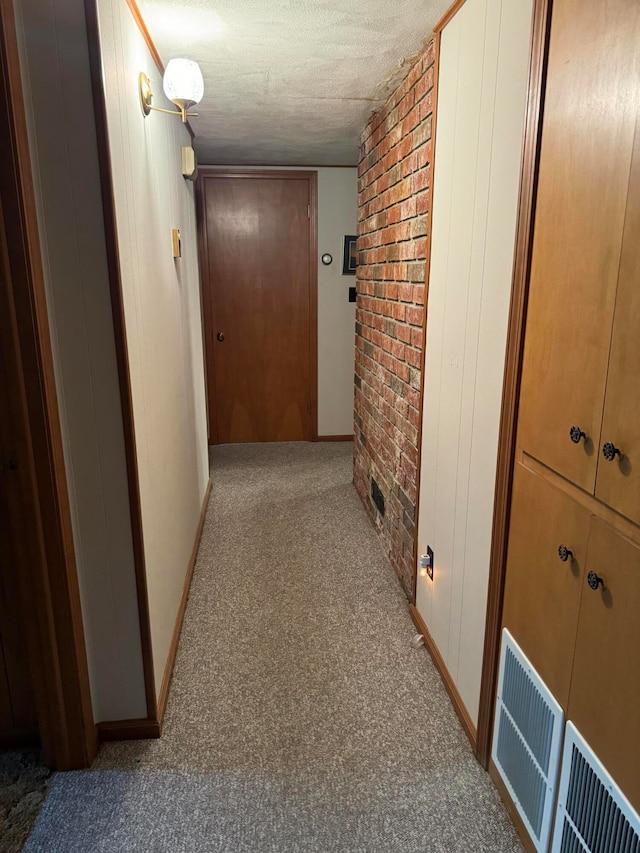 corridor with brick wall, light colored carpet, and a textured ceiling