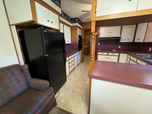 kitchen featuring dark countertops, wall oven, freestanding refrigerator, white cabinets, and under cabinet range hood