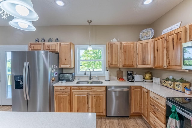 kitchen featuring light wood-type flooring, sink, pendant lighting, appliances with stainless steel finishes, and a textured ceiling