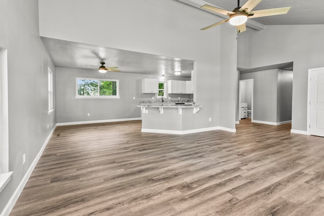 unfurnished living room with ceiling fan, light wood-type flooring, a textured ceiling, and high vaulted ceiling