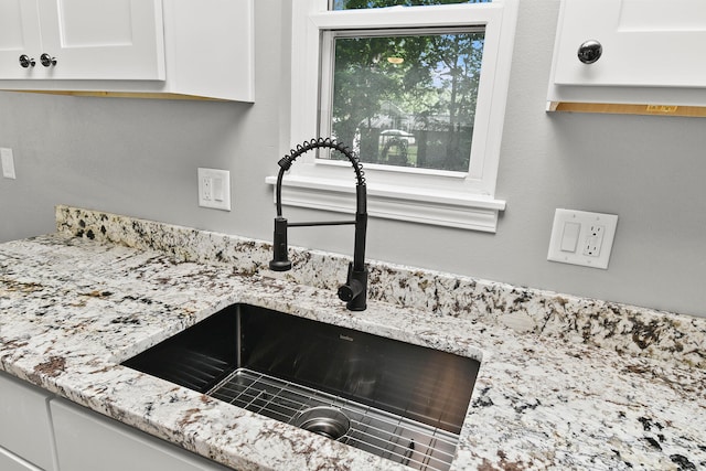 room details featuring light stone counters, white cabinetry, and sink