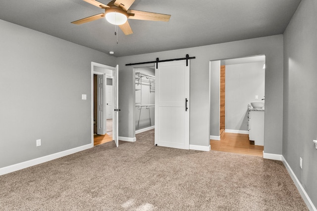 unfurnished bedroom featuring a barn door, light carpet, and ceiling fan