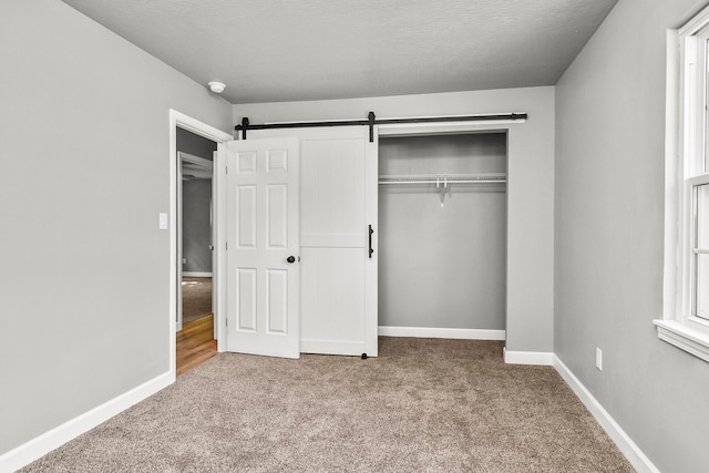 unfurnished bedroom with a barn door, light carpet, a closet, and a textured ceiling