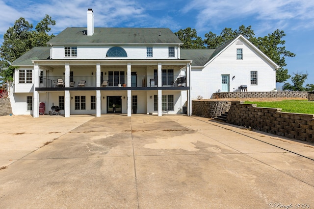 back of property with stairs, a patio area, a chimney, and a balcony
