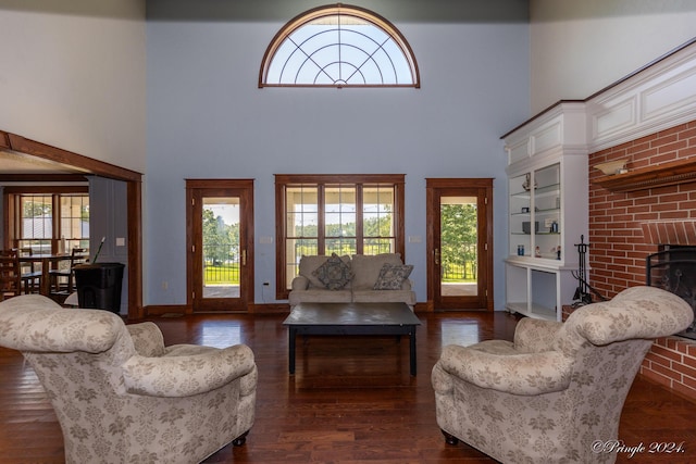 living area featuring wood finished floors, baseboards, a brick fireplace, and a towering ceiling