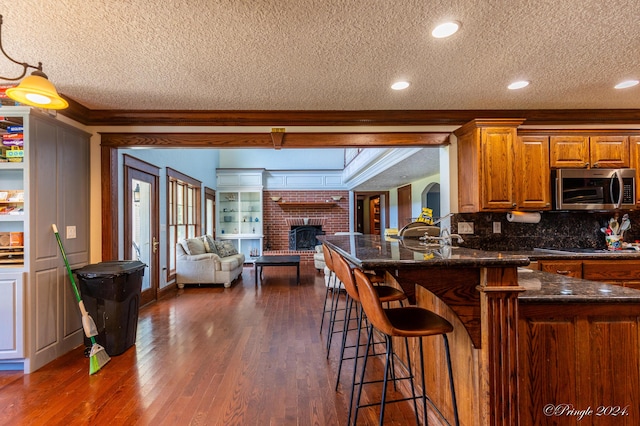 kitchen featuring a brick fireplace, a textured ceiling, stainless steel microwave, and crown molding