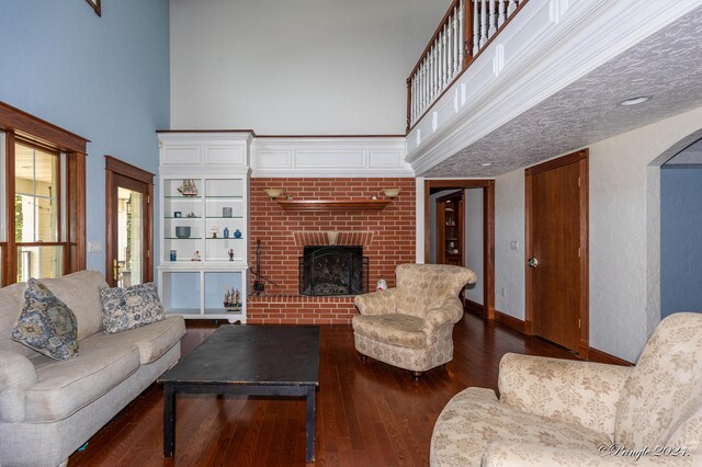 living room featuring arched walkways, baseboards, a brick fireplace, a high ceiling, and hardwood / wood-style floors