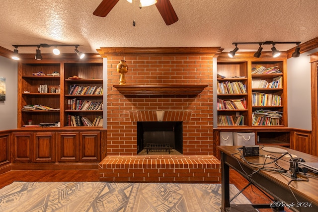 interior space with a textured ceiling, built in shelves, a brick fireplace, ceiling fan, and rail lighting