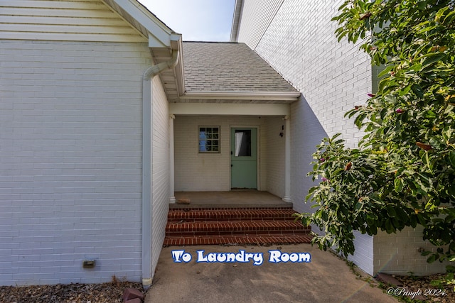 doorway to property featuring brick siding and roof with shingles