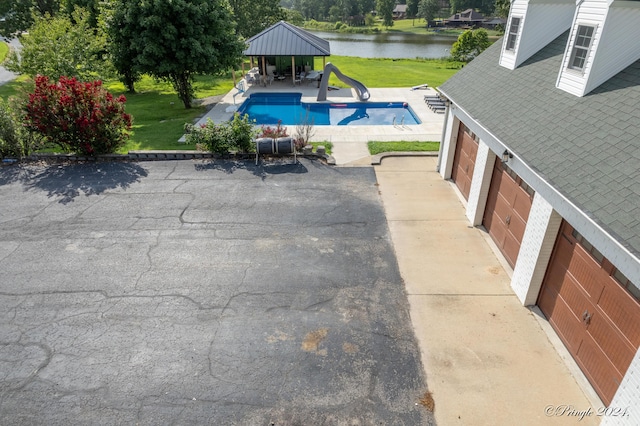 view of pool with a fenced in pool, a water slide, a water view, a lawn, and a gazebo