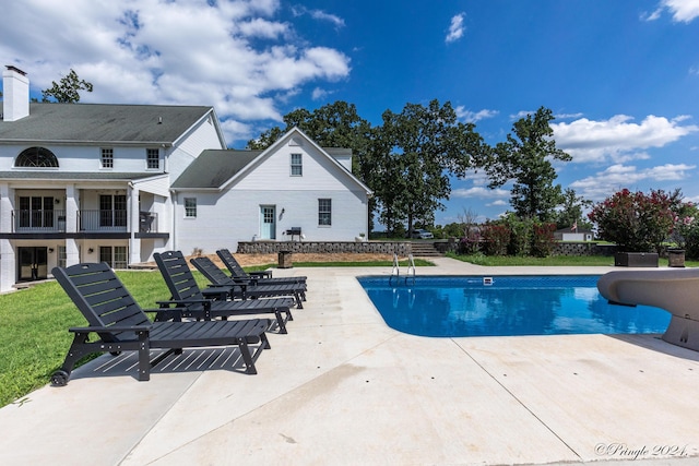 outdoor pool with a water slide, a yard, and a patio