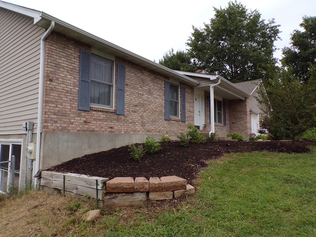 view of side of home with an attached garage, a lawn, and brick siding