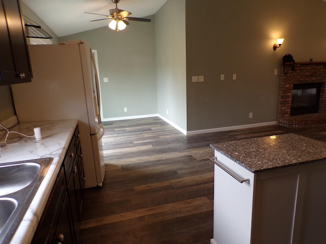 kitchen featuring dark wood-style floors, a fireplace, lofted ceiling, a ceiling fan, and baseboards