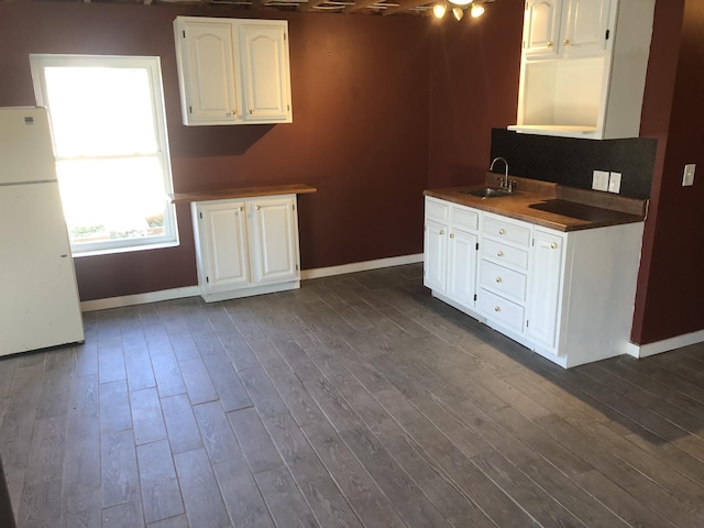 kitchen with a sink, baseboards, white cabinets, freestanding refrigerator, and dark wood-style floors