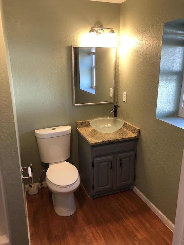 half bathroom with baseboards, a textured wall, toilet, wood finished floors, and vanity