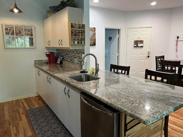 kitchen featuring light hardwood / wood-style floors, sink, stainless steel dishwasher, light stone countertops, and kitchen peninsula