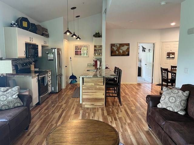 kitchen with light stone counters, pendant lighting, hardwood / wood-style flooring, stainless steel appliances, and a kitchen breakfast bar