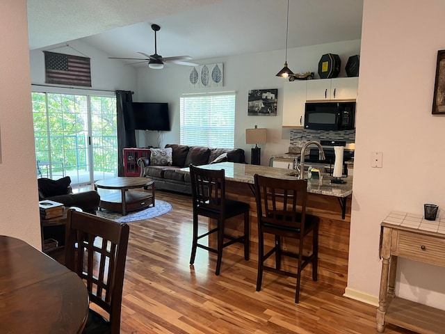 dining space with ceiling fan, sink, light hardwood / wood-style floors, and vaulted ceiling