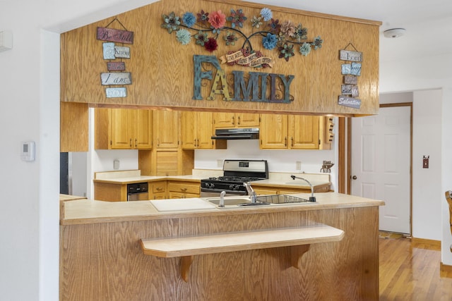 kitchen with gas stove, a breakfast bar area, light hardwood / wood-style flooring, sink, and kitchen peninsula