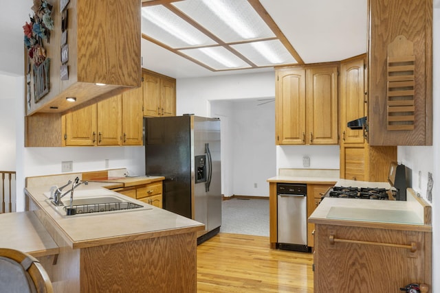 kitchen with light wood-type flooring, range, sink, kitchen peninsula, and stainless steel fridge with ice dispenser