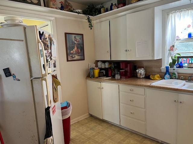 kitchen with white refrigerator, sink, and white cabinetry