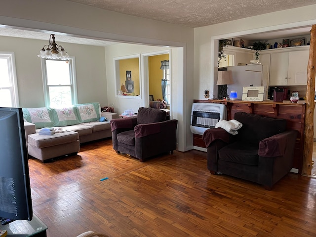 living room featuring heating unit, hardwood / wood-style floors, an inviting chandelier, and a textured ceiling