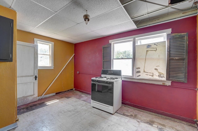 kitchen with light floors, baseboards, a drop ceiling, and white gas range oven