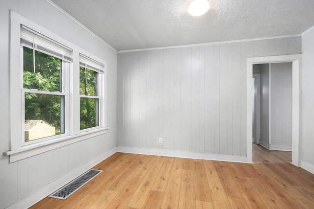 empty room with wood walls, ornamental molding, and light wood-type flooring