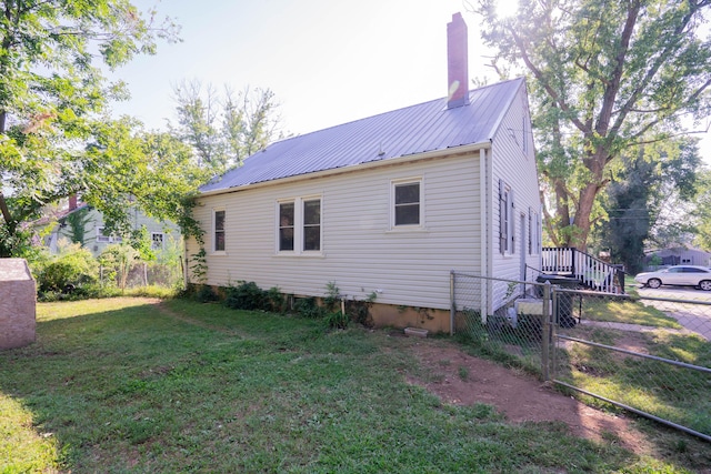 view of side of home featuring a chimney, fence, a yard, and metal roof