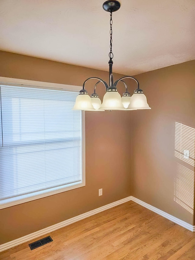 unfurnished dining area with an inviting chandelier and light wood-type flooring