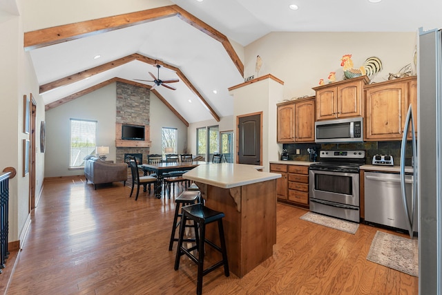 kitchen with ceiling fan, a kitchen island, light hardwood / wood-style flooring, beam ceiling, and appliances with stainless steel finishes